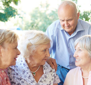 Senior friends having tea party in lovely summer cafe and sharing latest news with each other; two women putting arms on each others shoulders